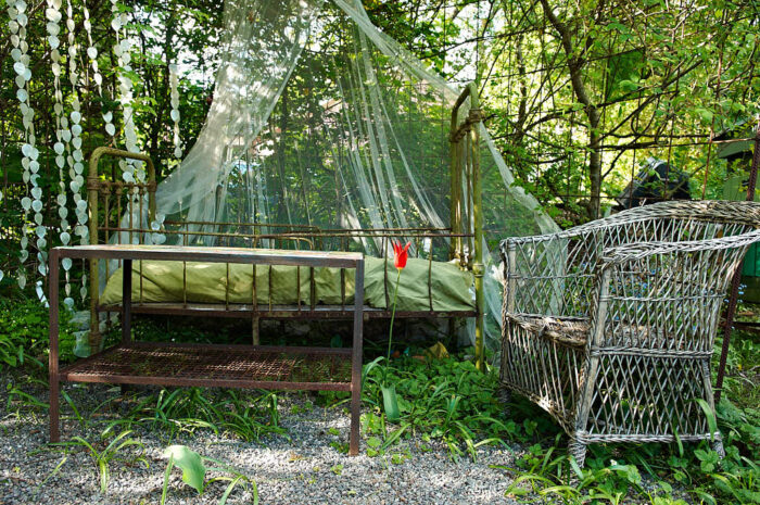 en sittgrupp av en gammal järnsäng, ett kakelklätt bord och en stol av rotting.