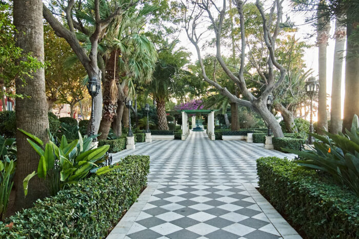 Plazoleta i Jardines del Paseo de Carlos III i Cádiz med svartvita plattor och ornamentala träd.
