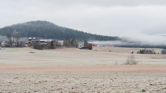 Frostbelagd åker med jordbruk och skogsklätt berg i bakgrunden.